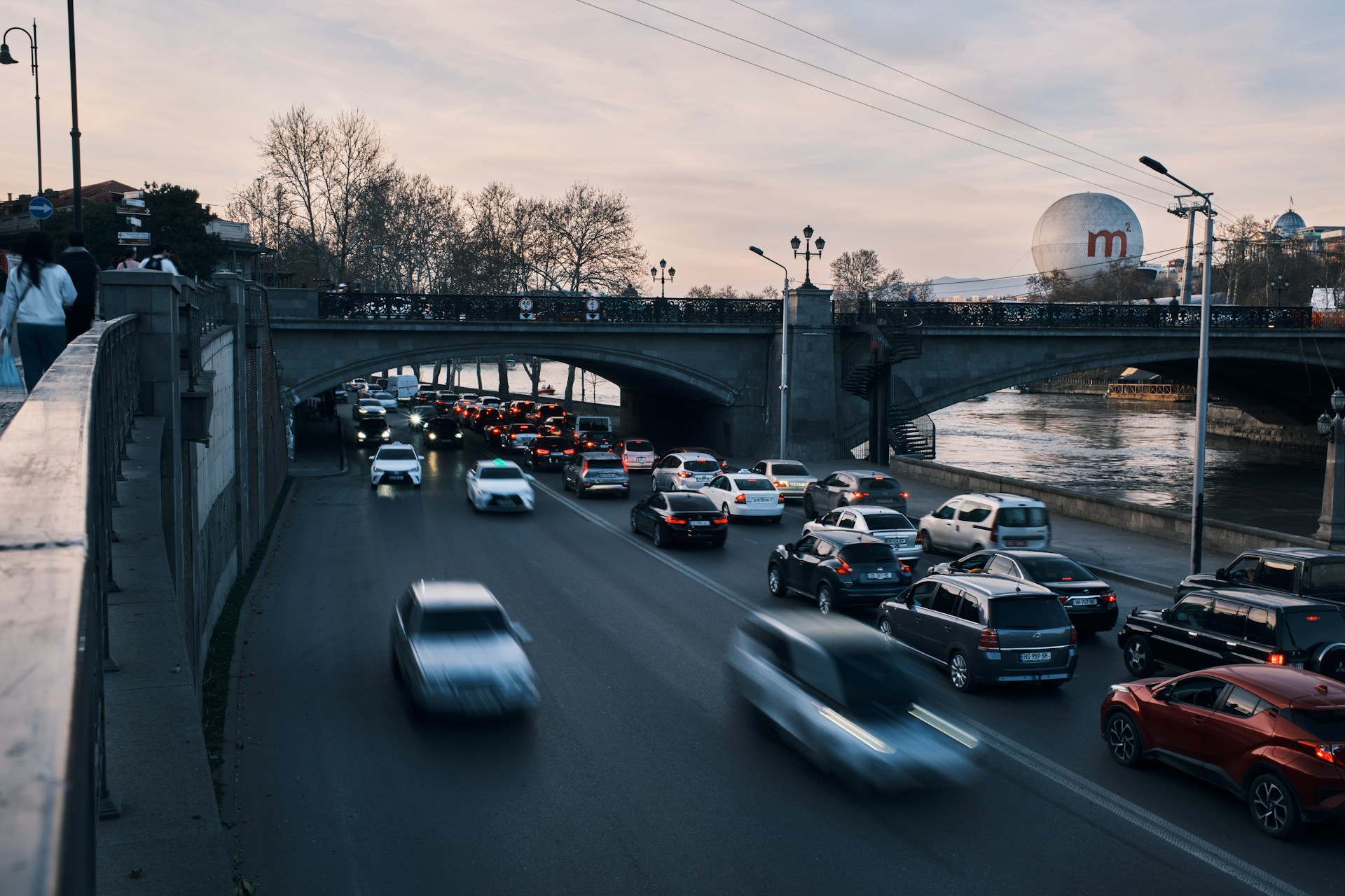 Riverside traffic beneath a bridge in Tbilisi at dusk